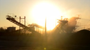 Maden ocağı. Gün batımında granit ocağında ezme tesisi. Crusher taş ocağında. Çok tozlu. Taş kırma. Sanayi tipi çakıl üretimi. Çakıl taşıyıcı. Koni tipi kaya öğütücü, parlayan güneş