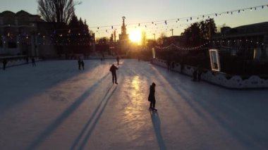 Kyiv Ukrayna, 3 Ocak 2022: İnsanlar gün batımında şehir parkında buz pateni pistinde paten kayıyor ve buz pistinde uzun gölgeler bırakıyor. Buz pateni pisti süslenmiş Yeni Yıl Noel aydınlatmaları süslemeler