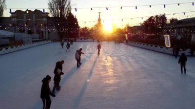 Kyiv Ukrayna, 3 Ocak 2022: İnsanlar gün batımında şehir parkında buz pateni pistinde paten kayıyor ve buz pistinde uzun gölgeler bırakıyor. Buz pateni pisti süslenmiş Yeni Yıl Noel aydınlatmaları süslemeler