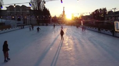 Kyiv Ukrayna, 3 Ocak 2022: İnsanlar gün batımında şehir parkında buz pateni pistinde paten kayıyor ve buz pistinde uzun gölgeler bırakıyor. Buz pateni pisti süslenmiş Yeni Yıl Noel aydınlatmaları süslemeler