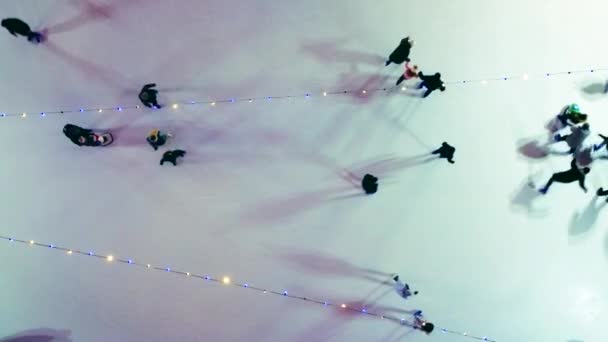 冬の夜景を眺めながら屋外でアイススケートを楽しむ人もいます 空中ドローンビュー 発光輝くガーランドランプの照明 長い影を投げなさい クリスマスのお祝いの休日のレクリエーション — ストック動画