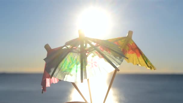 青い空を背景に3枚の紙の傘を手に持つ男は 青い海の表面に明るく輝く太陽と日当たりの良いパスをカクテル装飾 観光の概念 — ストック動画