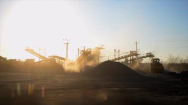 Maden ocağı. Gün batımında granit ocağında ezme tesisi. Crusher taş ocağında. Çok tozlu. Taş kırma. Sanayi tipi çakıl üretimi. Çakıl taşıyıcı. Koni tipi kaya öğütücü, parlayan güneş