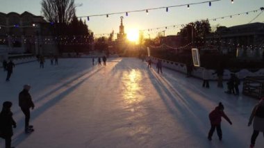 Kyiv Ukrayna, 3 Ocak 2022: İnsanlar gün batımında şehir parkında buz pateni pistinde paten kayıyor ve buz pistinde uzun gölgeler bırakıyor. Buz pateni pisti süslenmiş Yeni Yıl Noel aydınlatmaları süslemeler
