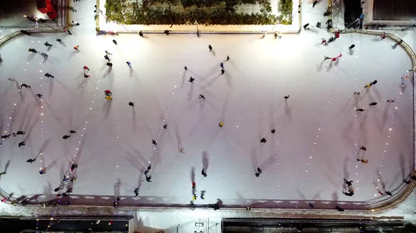 stock image People skating on ice skating rink outdoors on winter night top view. Aerial drone view. Luminous glowing garlands lamps lighting. Cast long shadows. New Year Christmas celebration holidays recreation