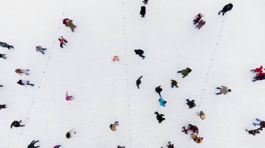 İnsanların kış günü geniş açık hava buz pateni pistinde kayışlarının en üst görüntüsü. Paten sahasında buz pateni yapan kalabalığın üzerinden hava aracı görüntüsü uçuşu. Kış sporları. Kaykay geçmişi. Şehir Buz Pisti.