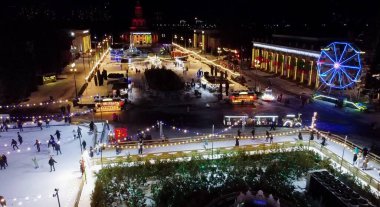 Birçok insan açık havada buz pateni pistinde paten kayıyor. Yılbaşı süsleri, süslemeler, kış gecelerinde parlak çelenkler. Yeni yıl Noel kutlaması. Havadan