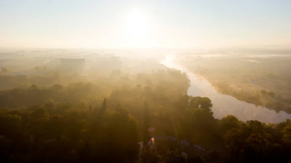 stock image Forest park trees, river and many high-rise buildings in city in early morning at dawn in summer. Brightly shining sun, clear cloudless sky and morning mist Sunbeams and shadows Aerial drone landscape