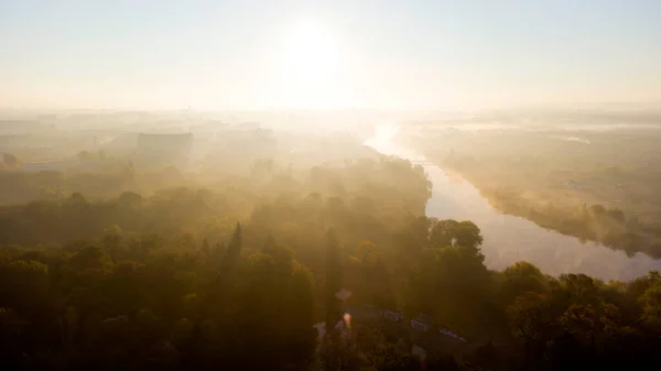 Stock image Forest park trees, river and many high-rise buildings in city in early morning at dawn in summer. Brightly shining sun, clear cloudless sky and morning mist Sunbeams and shadows Aerial drone landscape