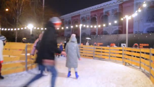 模糊的背景 许多人在露天溜冰场上滑冰 在冬夜的城市装饰着明亮的假日花环 圣诞假期及康乐活动背景 — 图库视频影像