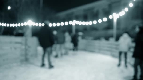 背景多くの人が冬の夜に街の明るい休日のガーランドを飾るオープンエアのアイススケートリンクでスケートします クリスマスお祝いの休日レクリエーション背景青の色 — ストック動画