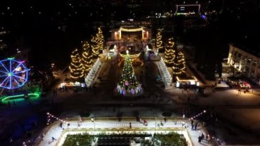 Noel ağacı ve insanlar açık havada buz pateni pistinde paten kayıyor. Yılbaşı süsleri, kış gecelerinde parlak çelenkler. Yeni yıl Noel kutlaması. Havadan