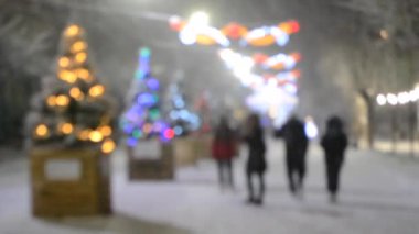 Yürüyen insanlar kış gecesi yoğun kar yağışında birçok Noel ağacı süslediler. Noel tatilleri kutlar. Dekorasyon sokak süsleri sokak ışıklandırması. Bulanık arkaplan