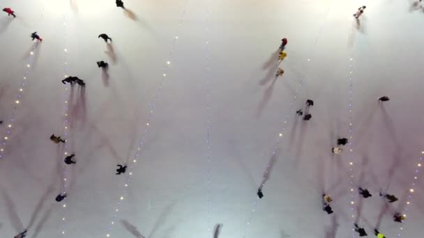 人们在冬夜山顶的室外溜冰场上滑冰 空中无人驾驶飞机视图 灯火通明 圣诞佳节的娱乐活动 往下掉 — 图库视频影像
