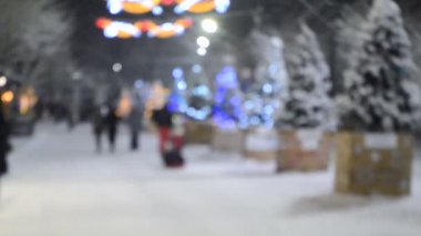 Bir adam kış gecesinde Noel ağaçları ve aydınlatmalarla süslenmiş bir sokakta çocukları kızakla kayıyor. Soyut Noel Yeni Yıl arkaplanı.