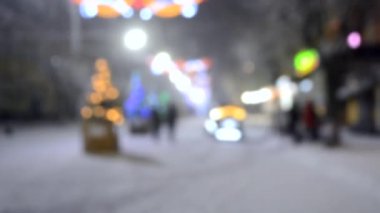 Noel ağaçları, aydınlanma ve kış gecelerinde yoğun kar yağışında yürüyen insanlarla dolu caddede yürüyen bir araba. Şehir sokağı. Soyut Noel Yeni Yıl arkaplanı.