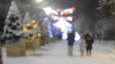 Noel ağacıyla sokakta yürüyen aile, aydınlatmalar, kış gecelerinde yoğun kar yağışında aydınlık sokak dekorasyonları. Bulanık arkaplan. Noel, yeni yılı kutluyor