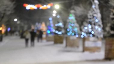 İnsanlar, kış gecesi yoğun kar yağışı sırasında sokakta parlak süslemeler, aydınlatmalar ve sokak süslemeleri ile süslenmiş Noel ağaçları boyunca yürürler. Yılbaşı. Bulanık arkaplan