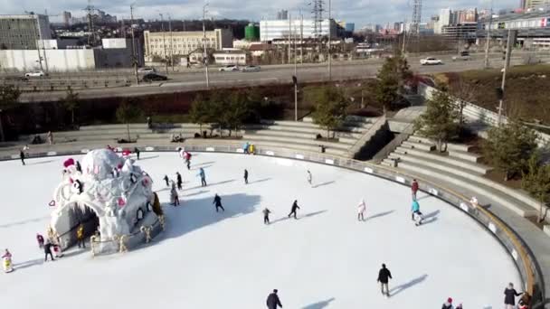 オープンエアのスケートリンク 道路橋や通過車 冬の晴れた日に多くの高層ビル 人々は公共の氷のリンクでスケート 都市景観 空中ドローンビュー — ストック動画