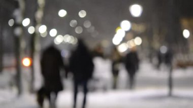 Kışın şehirde gece vakti bebek arabasıyla gezen aile. İnsanlar kar yağışı sırasında ışık saçan fenerlerle aydınlanan cadde boyunca yavaşça yürüyorlar. Kış şehri gece manzarası. Bulanık arkaplan