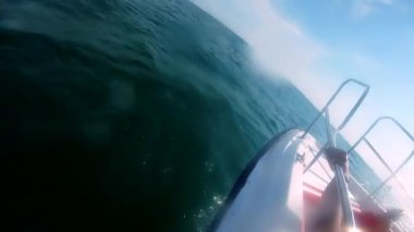 Güneşli bir yaz gününde insanların süratle yelken açtığı beyaz bir motorlu tekne. Sürat teknesi deniz dalgalarında zıplıyor. Yat motorlu teknesi hızlı denize yelken açıyor. Motorlu tekne ile seyahat eden turistler. Güneş suyun üzerinde parlıyor
