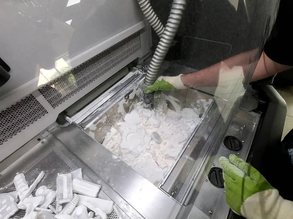 Male worker taking out models from white polyamide powder in working chamber of 3D printer, cleaning powder and putting on surface. Process of creating model on powder 3D printer. Multi Jet Fusion MJF