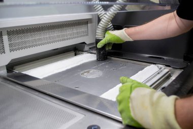 Bir erkek işçi, elektrikli süpürgeyle endüstriyel 3D yazıcının yüzeyini beyaz tozdan temizliyor. Çoklu Jet Füzyon MJF 3D baskı. Çalışma süreci. 3D yazdırma teknolojisi