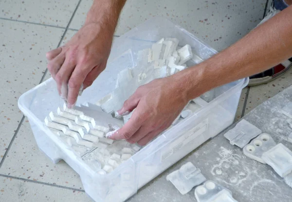 Male worker sorts through models in hands, lying in box and covered with white polyamide powder close-up. Objects printed on powder 3D printer. Technology Multi Jet Fusion MJF. 3D printing technology