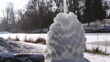 Güneşli bir kış gününde parkta buzlu çeşme. Donmuş suyla çeşme. Soğukta buzlu bir çeşmeden gelen bir su jeti. Gündüzleri arka plan buz ve karla kaplıydı.