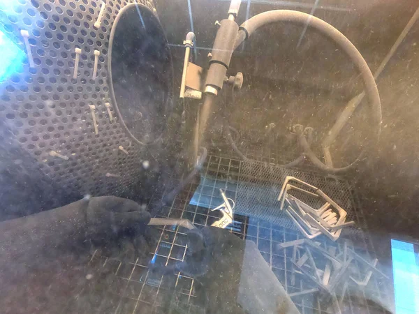 Shot blasting. Shot blasting of model printed on 3D printer from polyamide powder. A worker in sealed rubber gloves cleans the object by shot blasting in a shot blasting chamber. Industrial machine