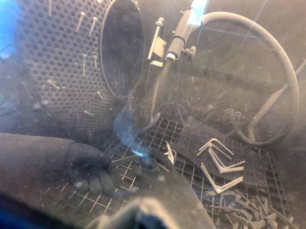 Shot blasting. Shot blasting of model printed on 3D printer from polyamide powder. A worker in sealed rubber gloves cleans the object by shot blasting in a shot blasting chamber. Industrial machine