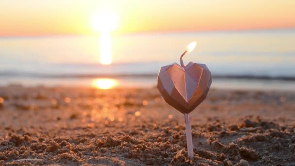 日没の夜明けの間に海の波の近くのビーチの砂の上で燃えるハート型のキャンドル 日の出を背景に砂の中の心の形でろうそくを燃焼 ロマンチックな恋愛ムード バレンタインデー — ストック動画