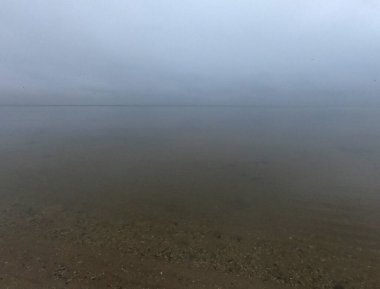 Sandy beach on calm sea. Calm sea cloudy weather. Smooth waveless sea surface in windless cloudy weather. Calmness. Rainy weather. Pure transparent water. Shoreline coast sea line. Natural background