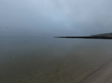 Sandy beach on calm sea. Calm sea cloudy weather. Smooth waveless sea surface in windless cloudy weather. Calmness. Rainy weather. Pure transparent water. Shoreline coast sea line. Natural background