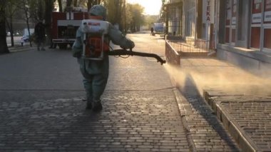 Man in airtight suit sprays disinfecting liquid a pavement on a street in the city against the backdrop of a sunset. Sanitation workers clean a crosswalk. Sanitary measures. coronavirus pandemic