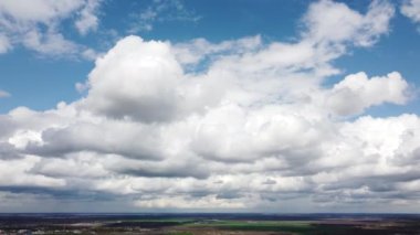 Fast movement of white cumulus clouds in blue sky during strong wind during day. Timelapse. Aerial drone view. Panoramic natural background. Rain. Rainy cloudy weather. Cloudscape. Scenic landscape.