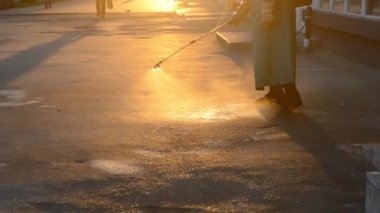 Man in airtight suit sprays disinfecting liquid a pavement on a street in the city against the backdrop of a sunset. Sanitation workers clean a crosswalk. Sanitary measures. coronavirus pandemic