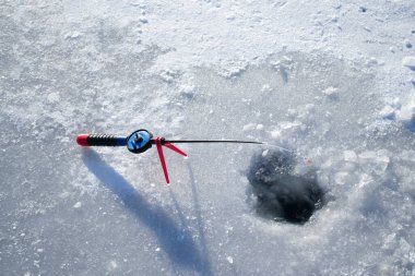 Winter ice fishing. Ice fishing in the winter. Small fishing rod stands near a hole in the ice of a river on a sunny day. Winter activity