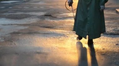 Man in airtight suit sprays disinfecting liquid a pavement on a street in the city against the backdrop of a sunset. Sanitation workers clean a crosswalk. Sanitary measures. coronavirus pandemic