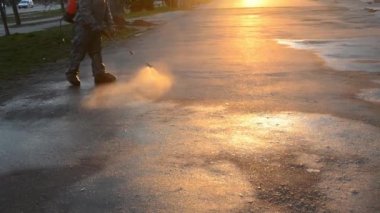 Man in airtight suit sprays disinfecting liquid a pavement on a street in the city against the backdrop of a sunset. Sanitation workers clean a crosswalk. Sanitary measures. coronavirus pandemic