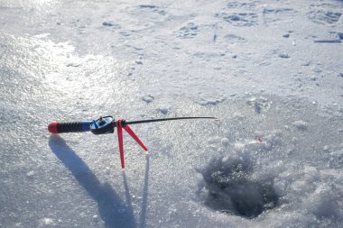 Winter ice fishing. Ice fishing in the winter. Small fishing rod stands near a hole in the ice of a river on a sunny day. Winter activity