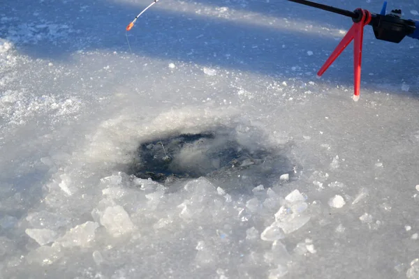 Winter ice fishing. Ice fishing in the winter. Small fishing rod stands near a hole in the ice of a river on a sunny day. Winter activity