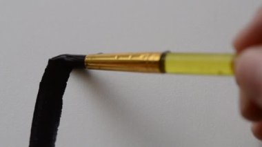 Person applies liquid black paint with brush on a white canvas close-up. Man painting with liquid gouache on canvas. The artist making brush strokes with paint on white paper. Creativity drawing art