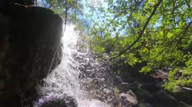 Waterfall shining with bright sun in park on sunny day. Drops of water from a current waterfall fall against the bright sun. Waterfall, cascade, fall. Natural bright vibrant background. Slow motion