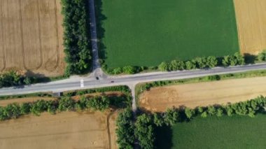 Automobile asphalt road with cars driving between agricultural fields with yellow ripened wheat and different green agricultural crops. Aerial drone view. Agricultural agrarian crop landscape Rotation