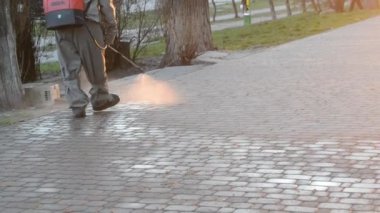 Man in airtight suit sprays disinfecting liquid a pavement on a street in the city against the backdrop of a sunset. Sanitation workers clean a crosswalk. Sanitary measures. coronavirus pandemic