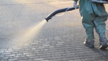 Man in airtight suit sprays disinfecting liquid a pavement on a street in the city against the backdrop of a sunset. Sanitation workers clean a crosswalk. Sanitary measures. coronavirus pandemic