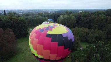 Balloon Festival. Inflating big balloon aerostat. Several balloons lie on ground and inflate in clearing in forest. Entertainment rest, recreation, travelling. Aerial drone view. Lifting up, rising