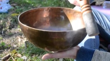 Person playing on Tibetan singing bowl closeup. Tibetan singing bowl sounding from vibration walls and edge by hand moving rotation wooden pestle. Buddhist meditation zen practice. Musical instrument