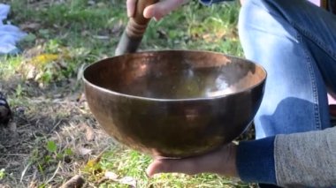 Person playing on Tibetan singing bowl closeup. Tibetan singing bowl sounding from vibration walls and edge by hand moving rotation wooden pestle. Buddhist meditation zen practice. Musical instrument